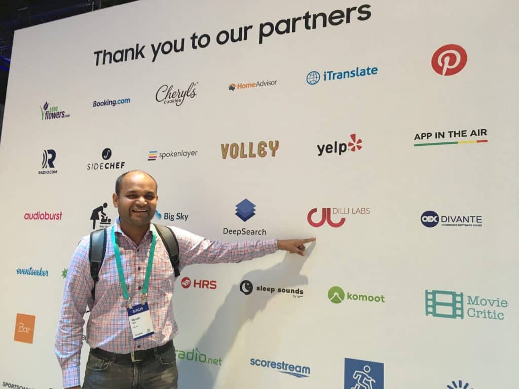 Dilli Labs founder Piyush Hari poses with Dilli Labs logo in background at Samsung Developer Conference 2019.